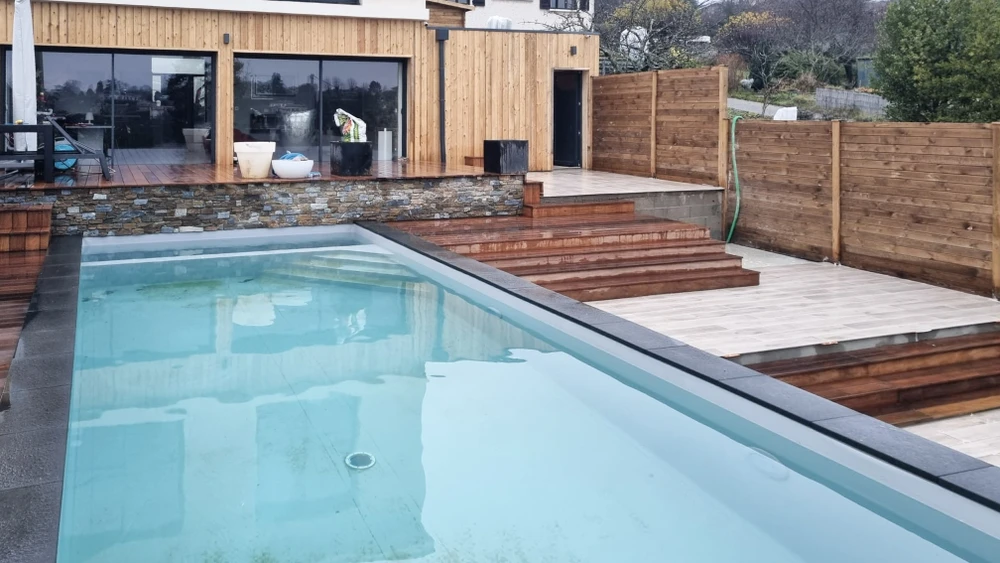 Jardin contemporain extérieur avec terrasse en bois composite, sculpture décorative en bois flotté sur lit de galets