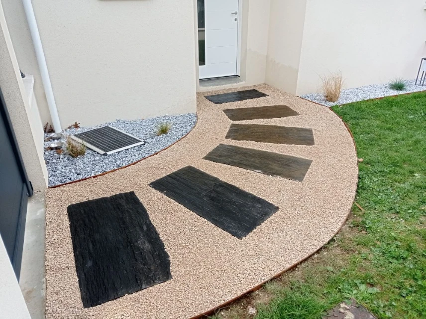 Jardin contemporain extérieur avec terrasse en bois composite, sculpture décorative en bois flotté sur lit de galets